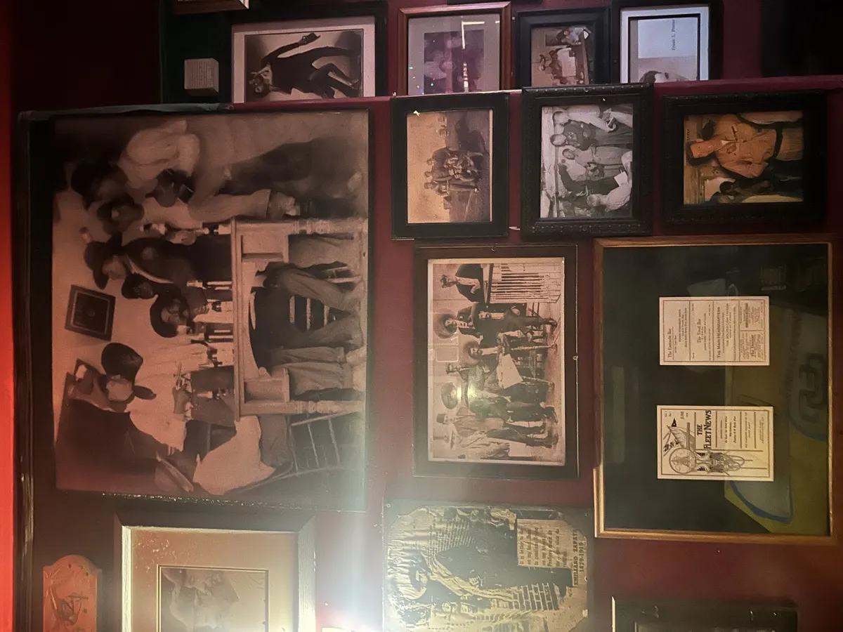 The photo wall inside Tivoli Bar and Grill, dense black and white historical photos and newspaper clippings covering a dark red wall